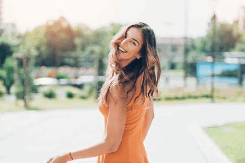 Woman with Brown hair and orange dress smiling in the street